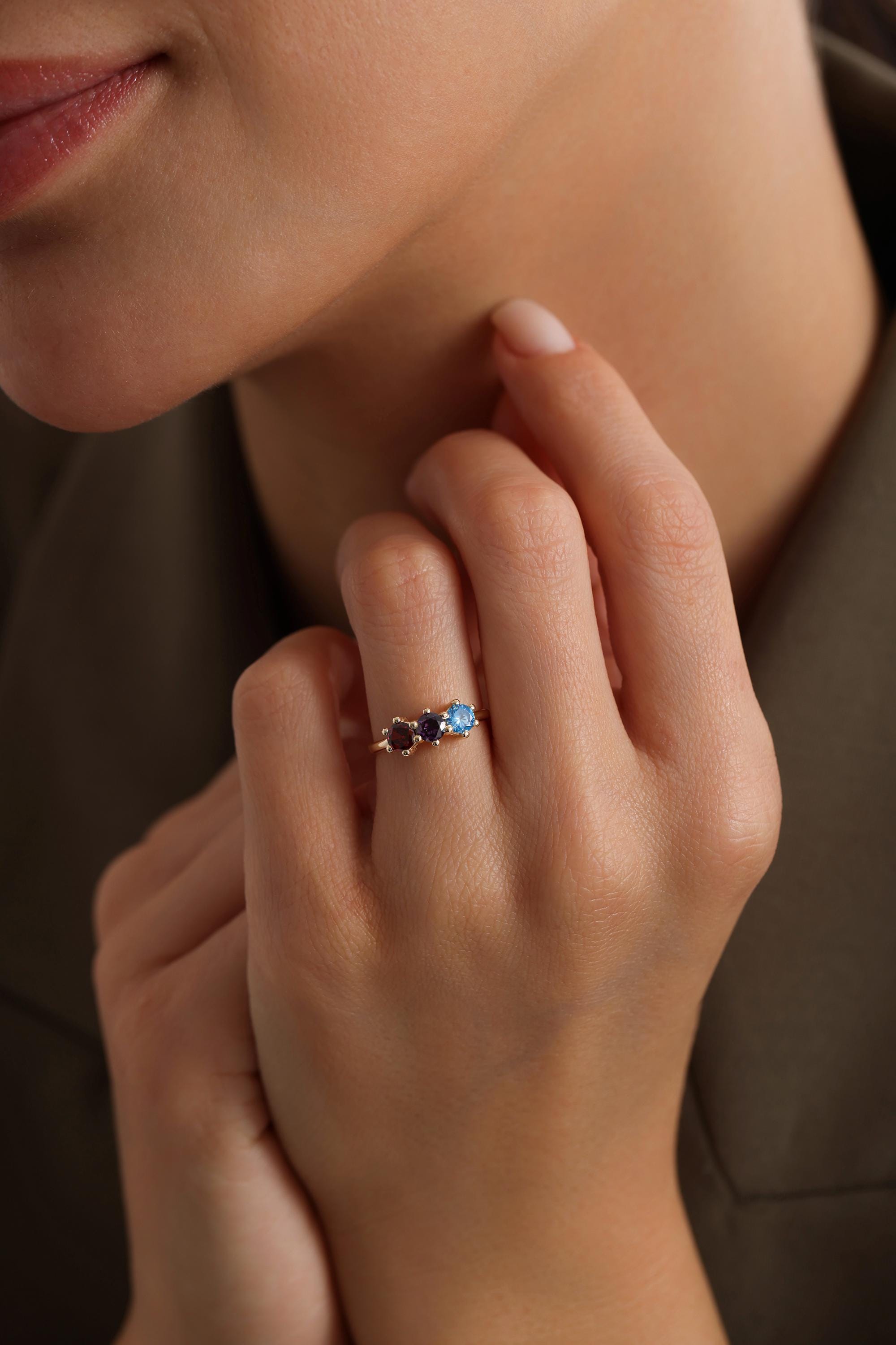 May include: A gold ring with three gemstones. The gemstones are a dark purple, a light purple, and a light blue.