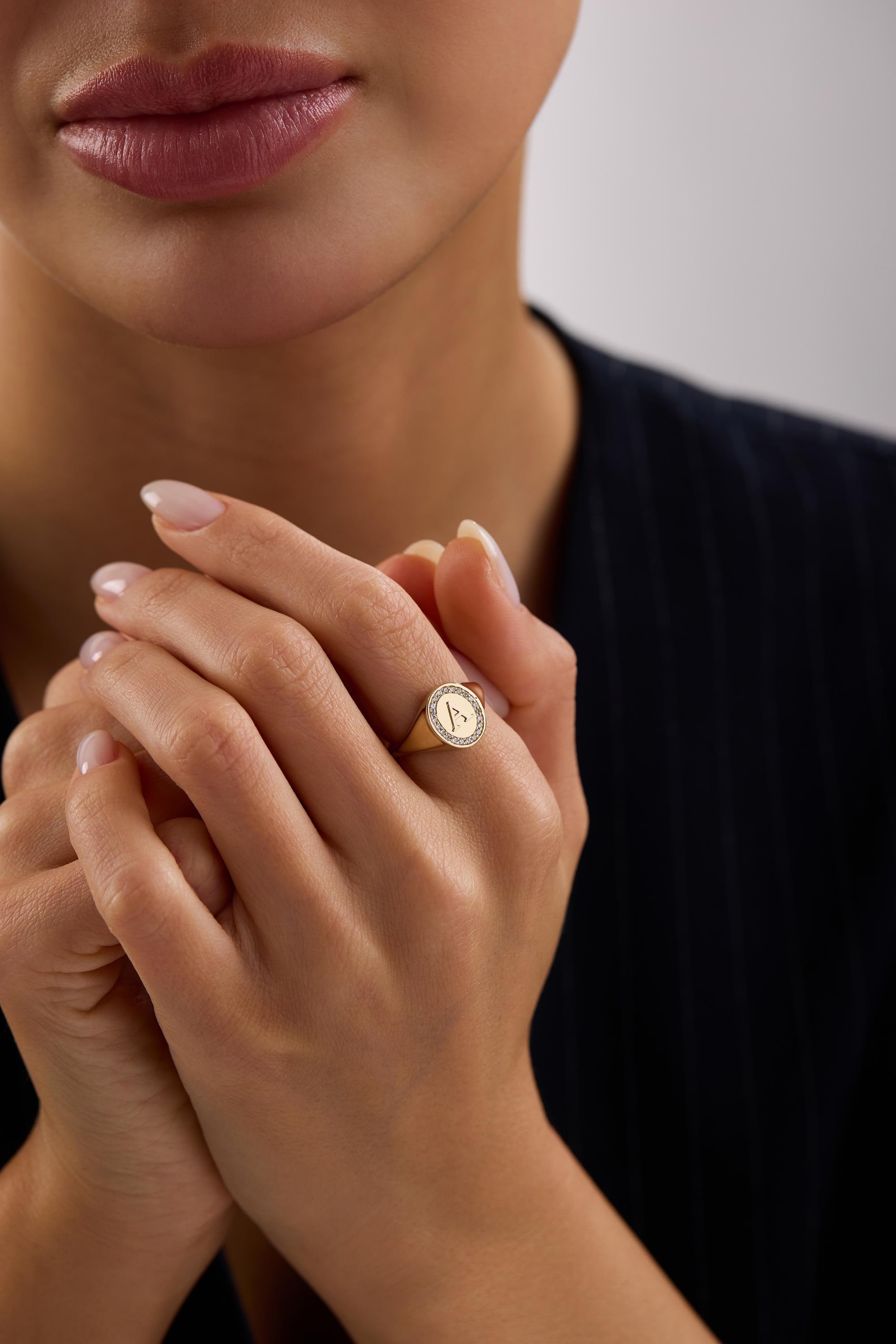 A close-up of a person's hand wearing a gold ring with a letter "A" on it, with their fingers crossed.