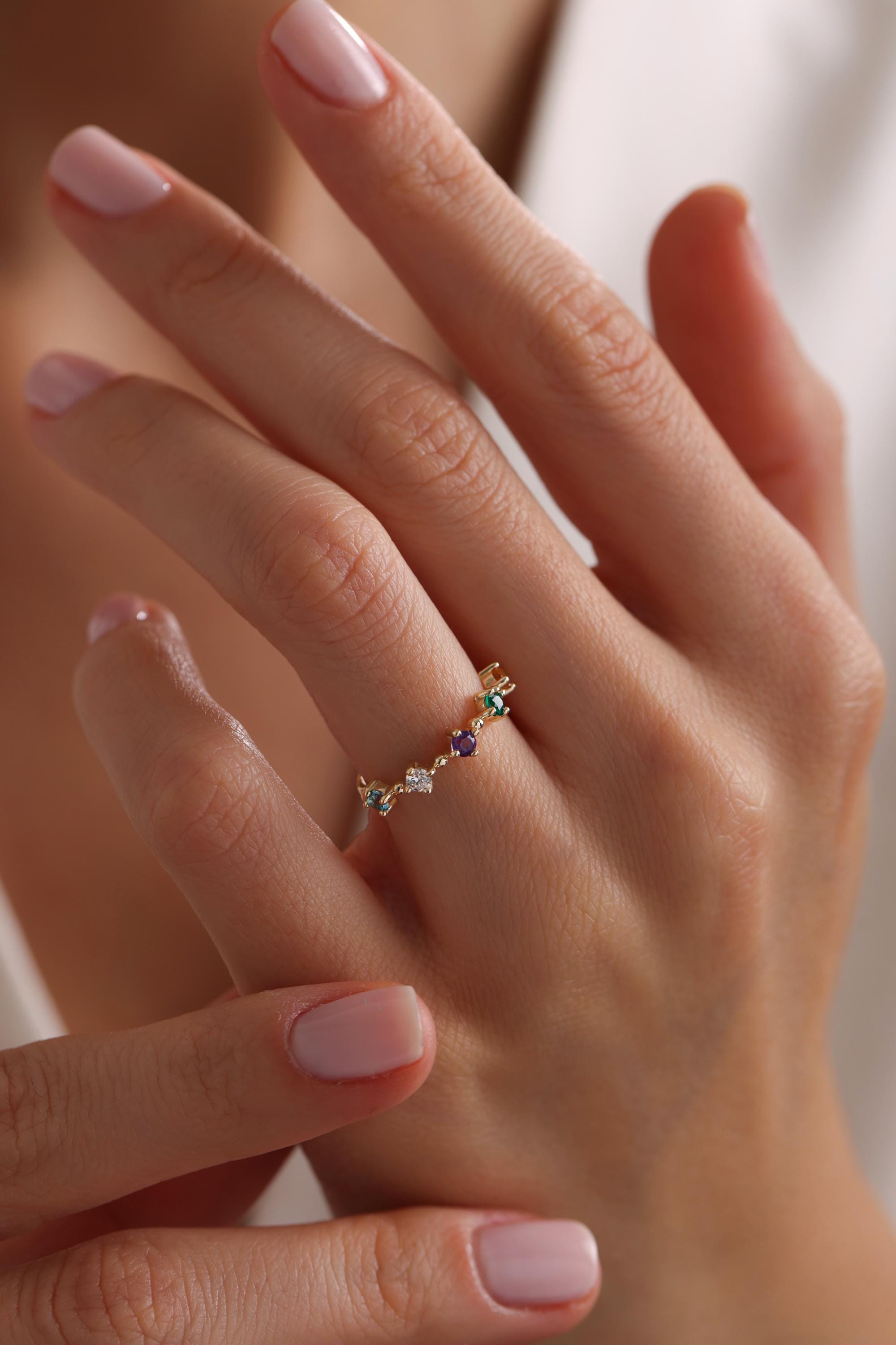 May include: A gold ring with a delicate chain design and five small gemstones: one purple, one green, one light blue, one clear, and one green.
