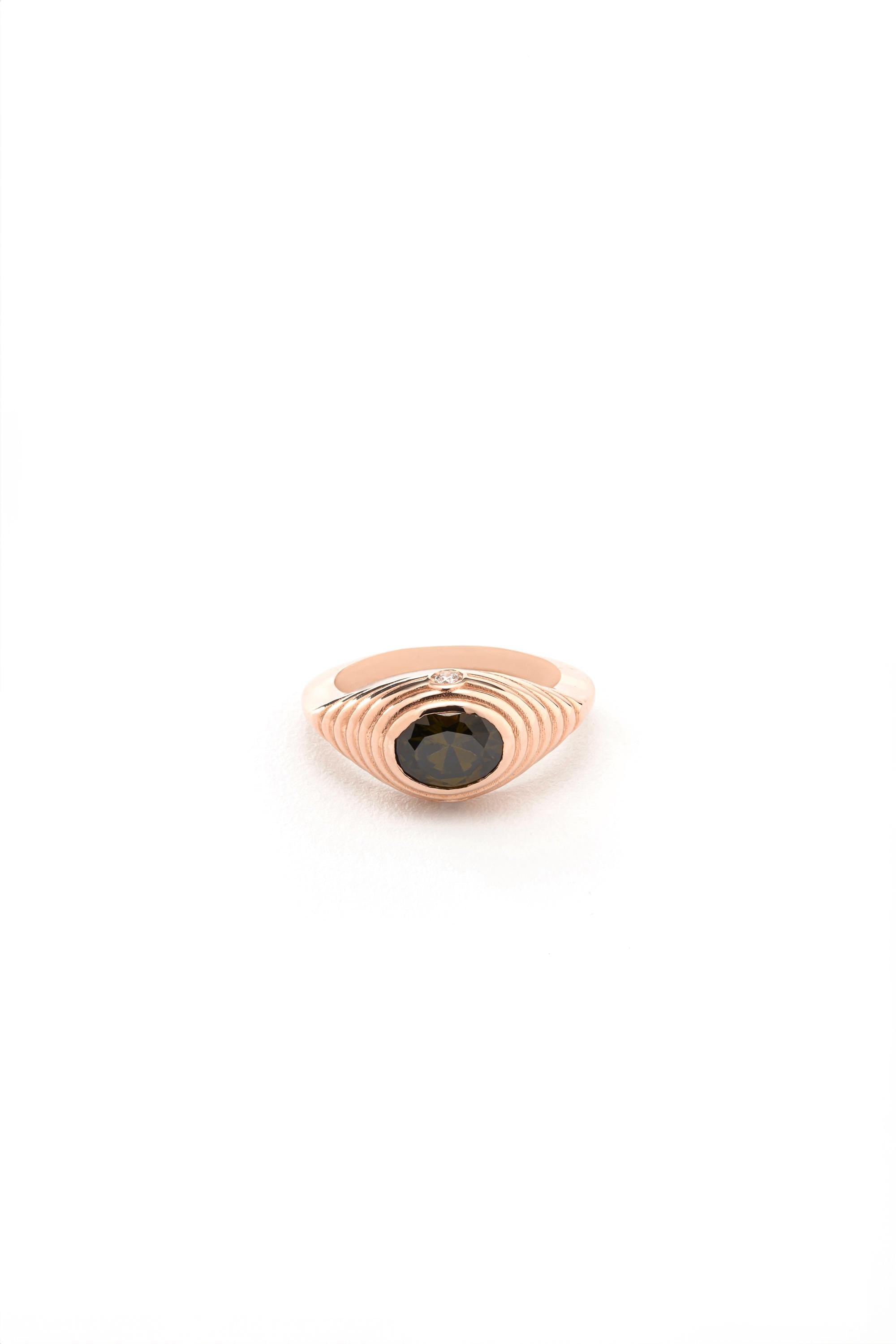 A rose gold ring with a dark green gemstone, possibly a sapphire or similar stone, set in the center of the ring.