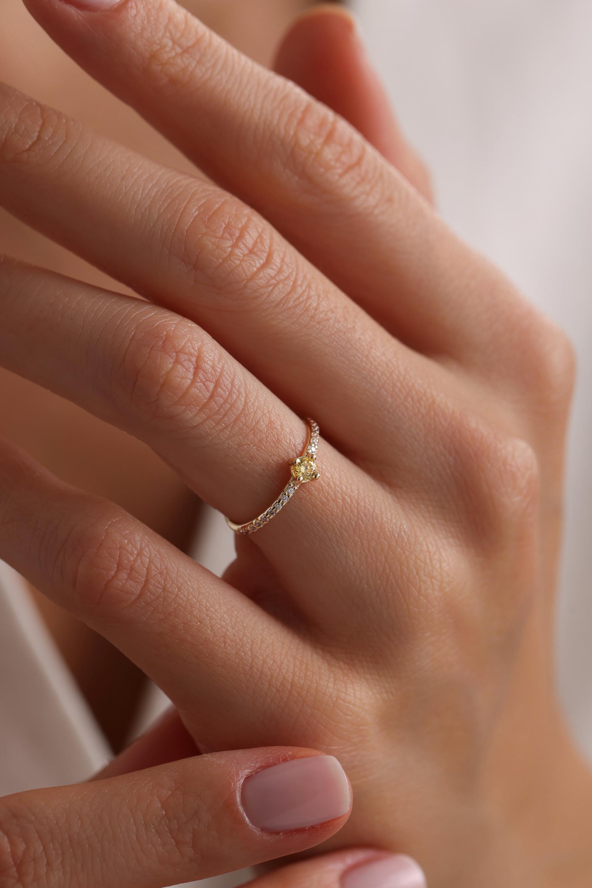 May include: A delicate gold ring with a small yellow gemstone set in the center and a row of tiny white gemstones around the band.