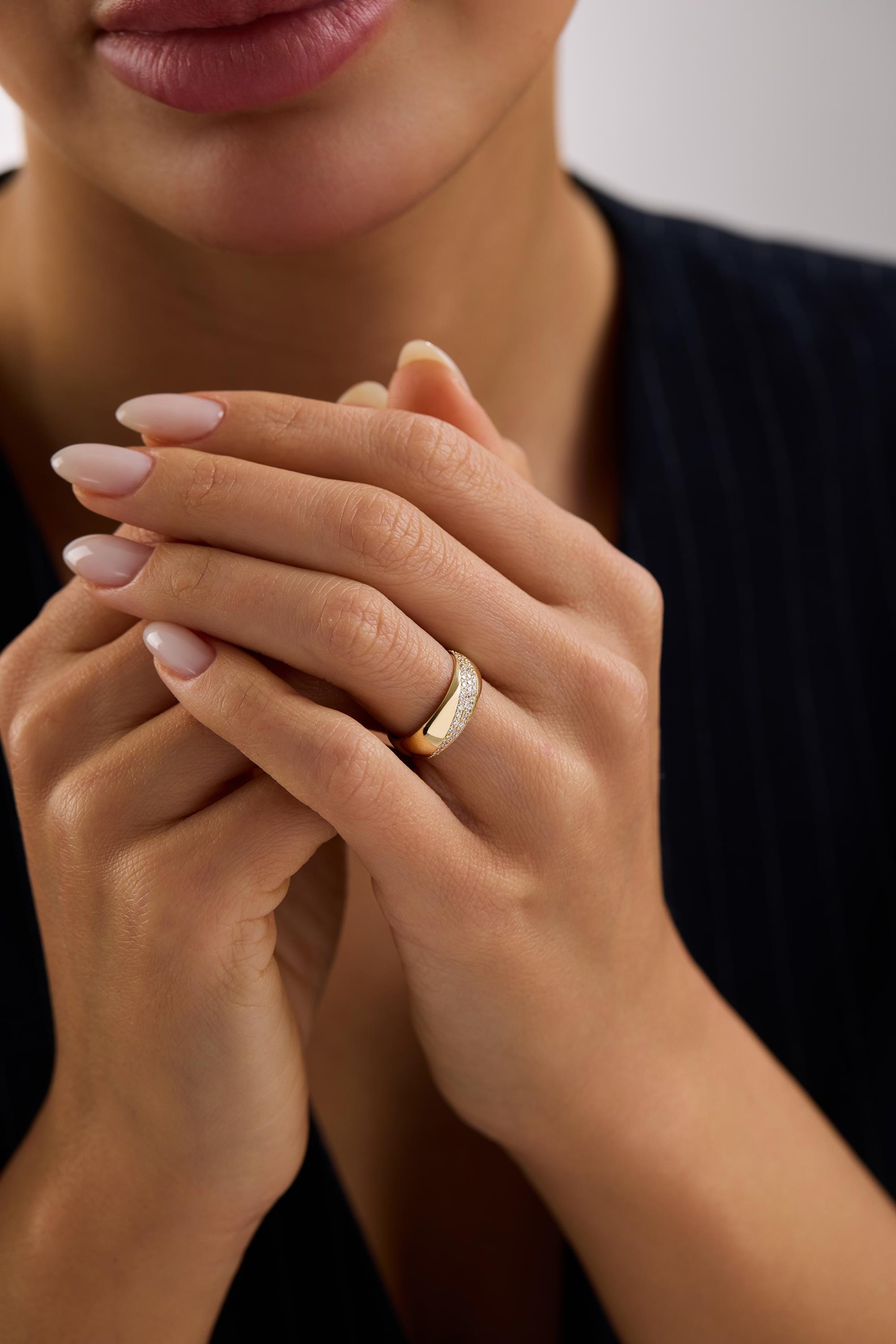 A close-up of a person's hands wearing a gold ring, with their fingers gently curled together.