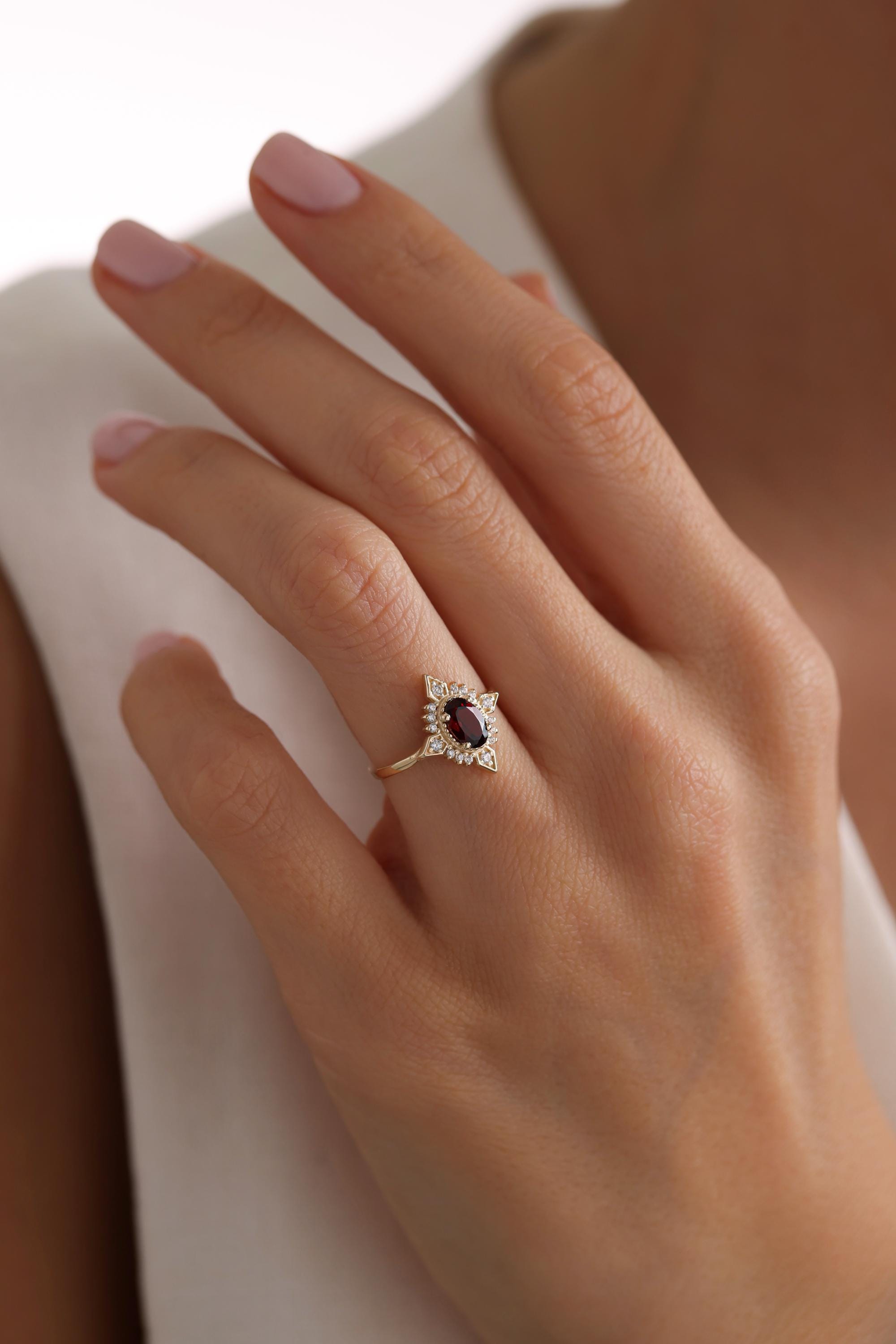 May include: A gold ring with a red oval gemstone surrounded by smaller white gemstones.
