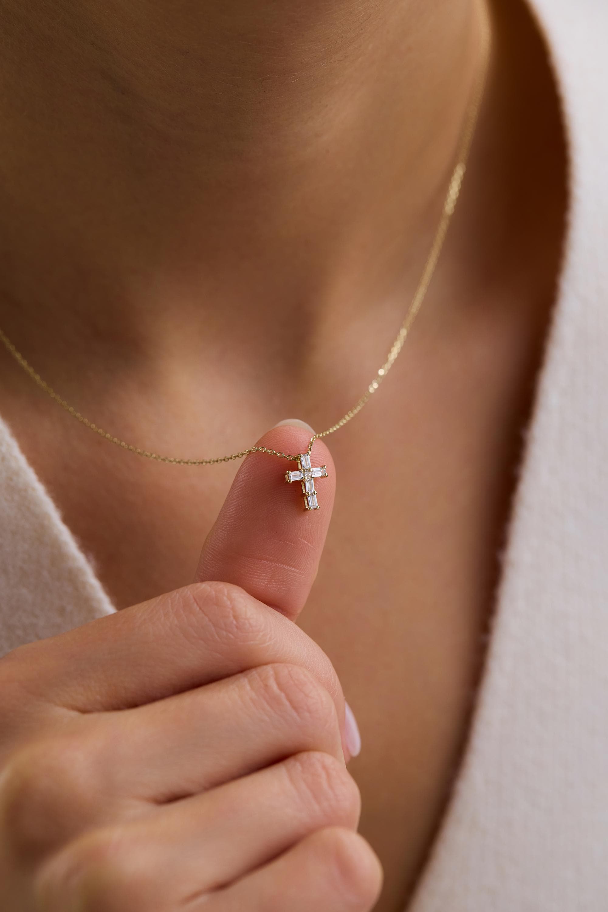 A close-up of a person's hand wearing a gold necklace with a small cross pendant.