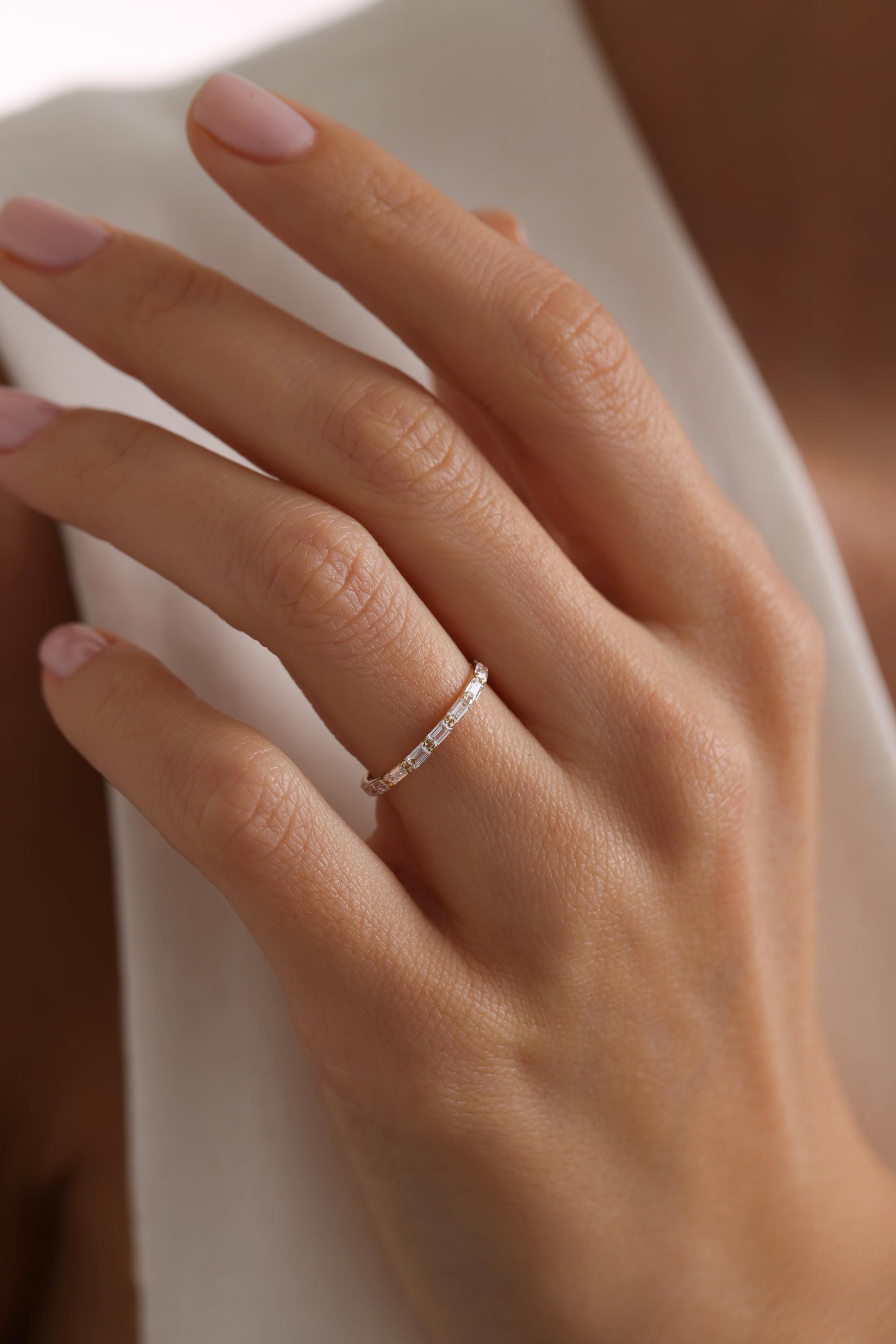May include: A thin gold band ring with small, clear, rectangular stones set in a pave setting.