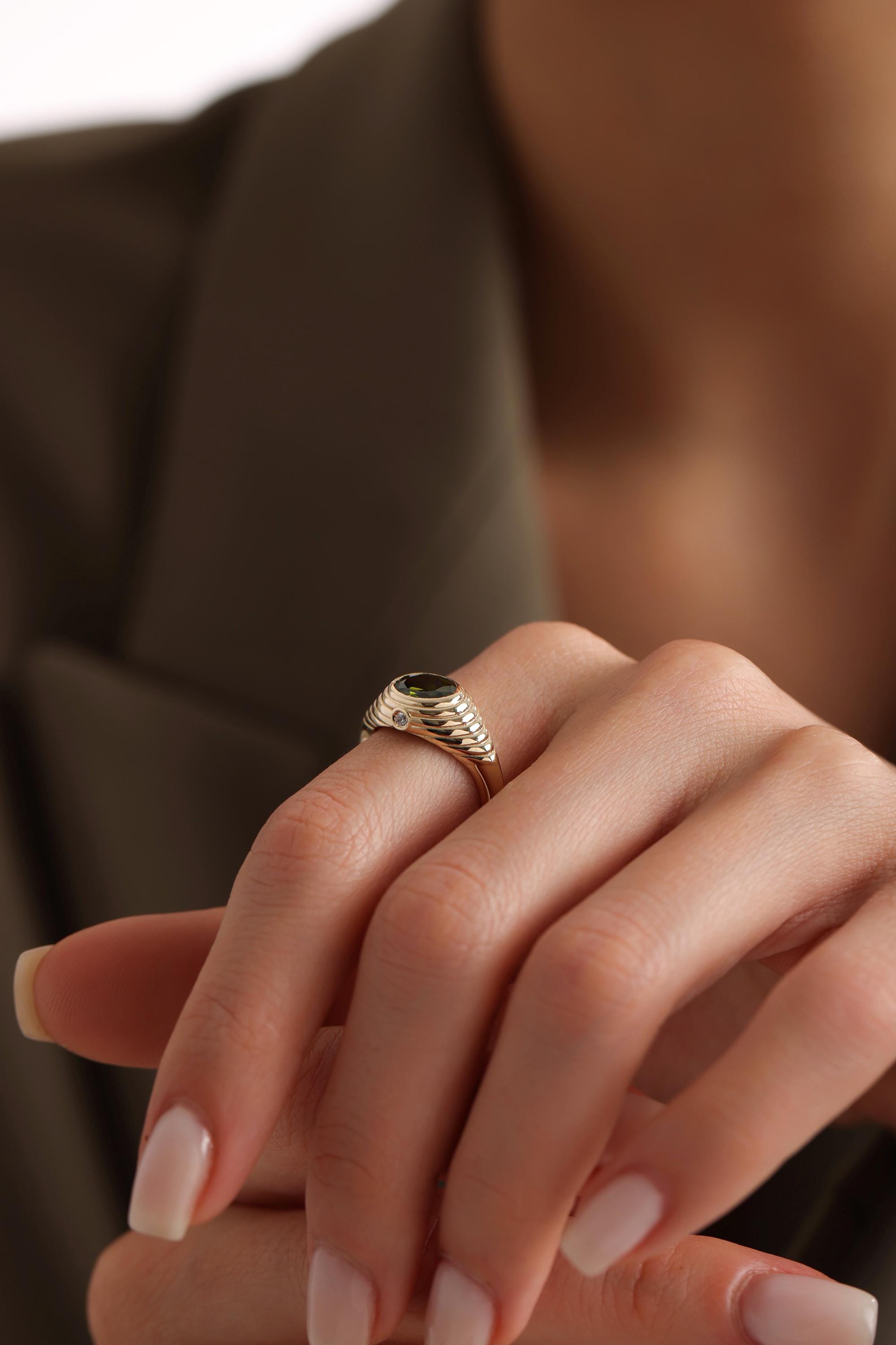 A close-up of a person's hand wearing a gold ring with a green gemstone.