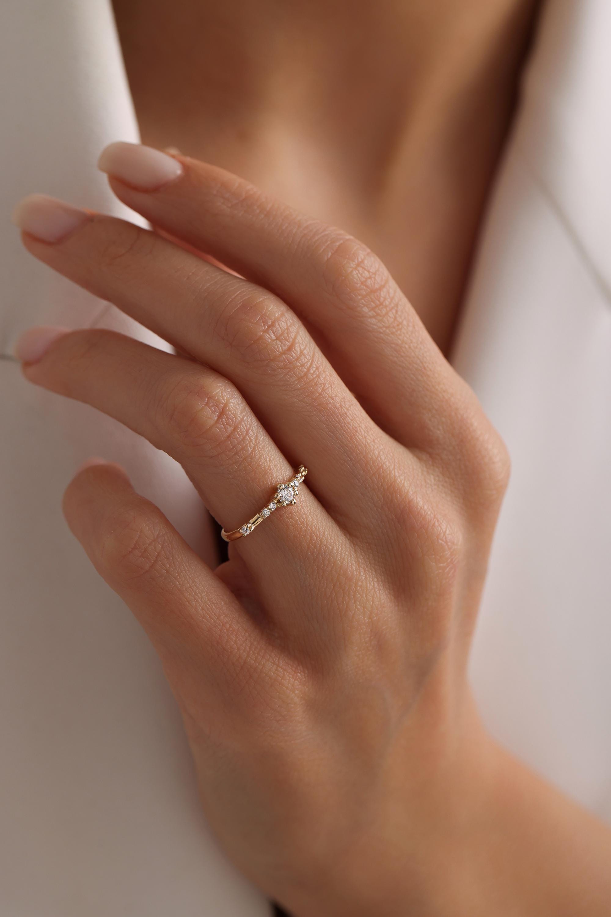 May include: A delicate gold ring with a small round diamond in the center and smaller diamonds set along the band.
