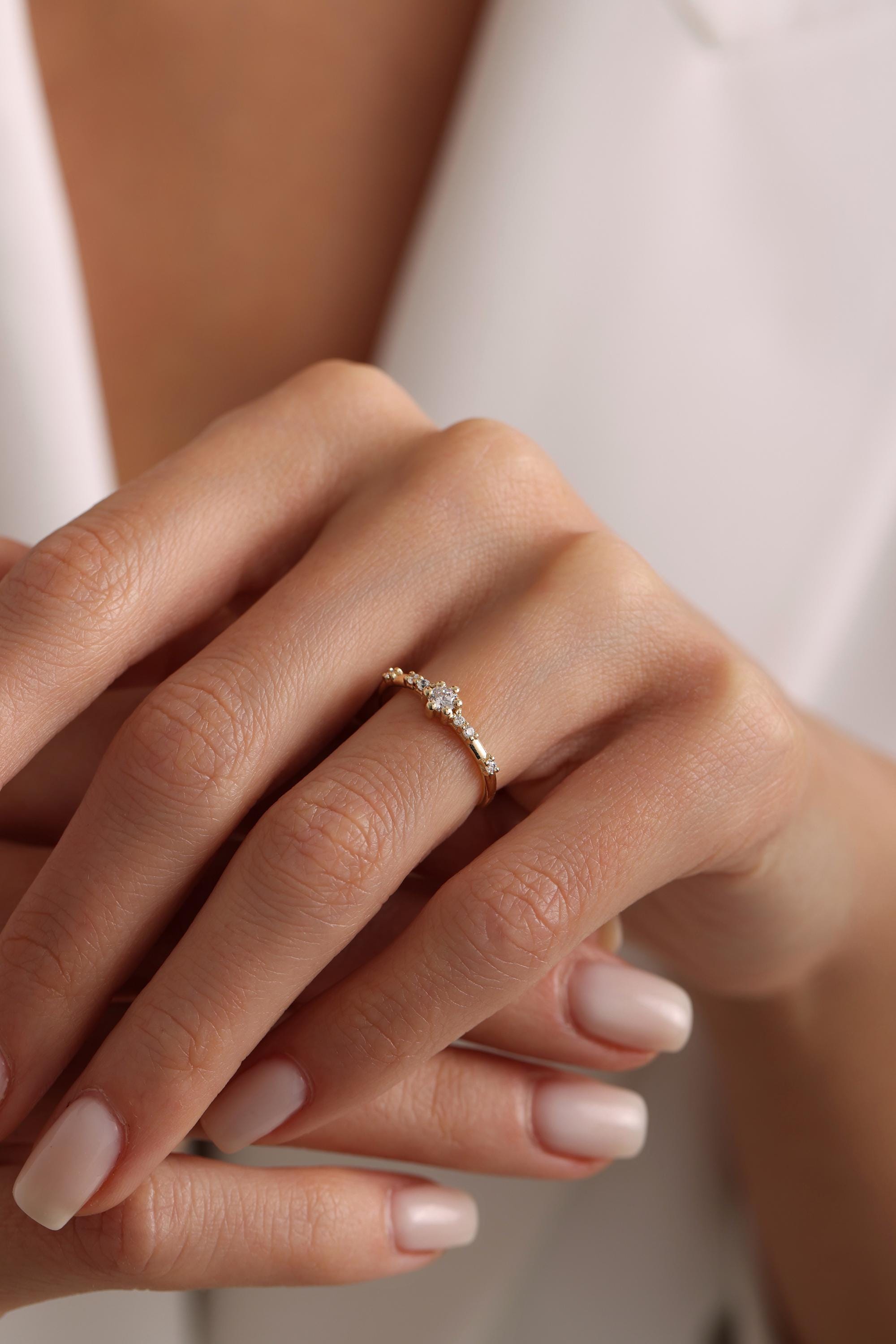 May include: A delicate gold ring with a small, clear diamond in the center and smaller diamonds on either side of the center stone.