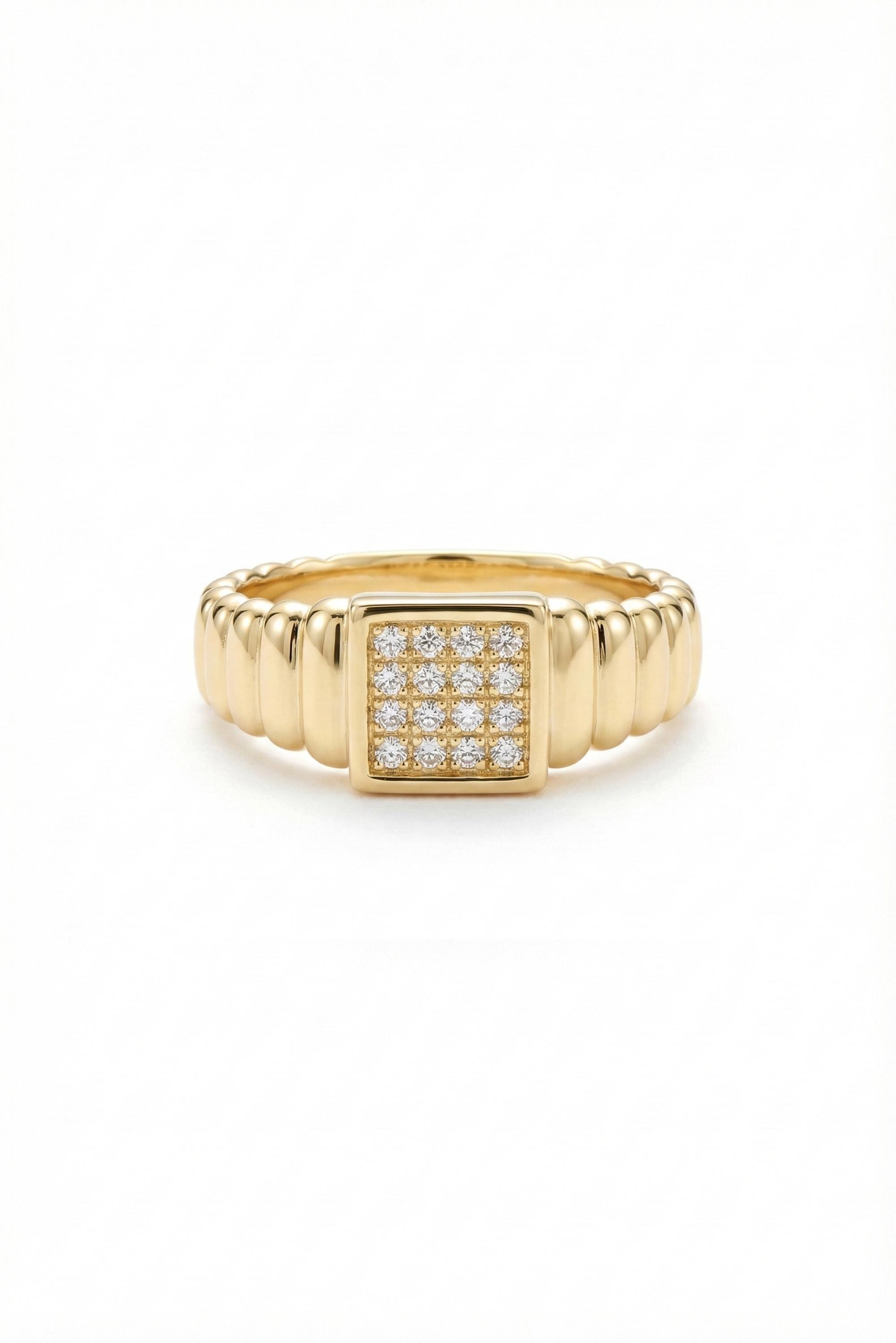 May include: A gold-colored ring with a square center featuring a cluster of small, clear stones. The band has a ribbed design, adding texture to the jewelry. The ring is set against a white background.