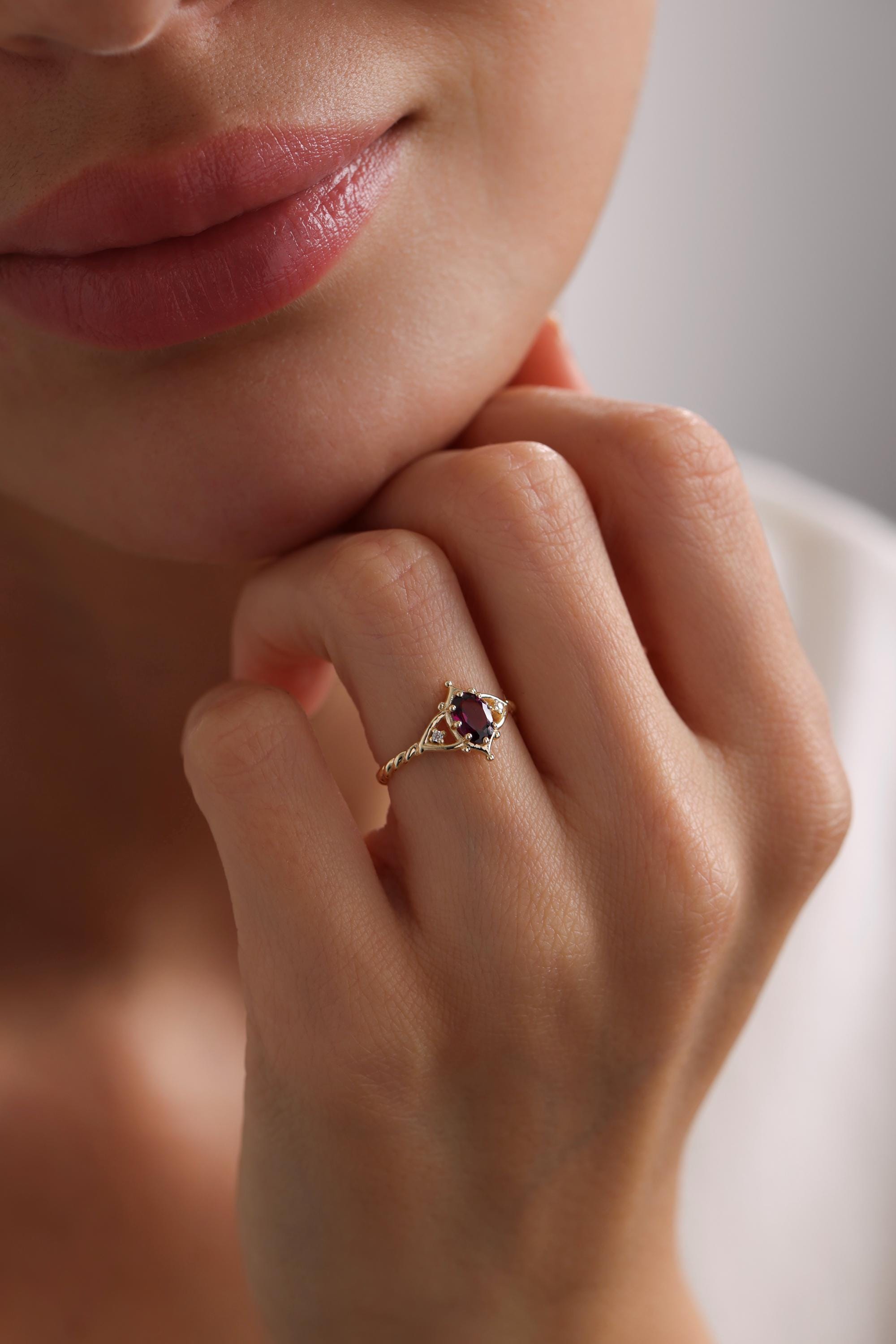 May include: A gold ring with a purple oval gemstone surrounded by smaller clear gemstones. The ring has a twisted band.