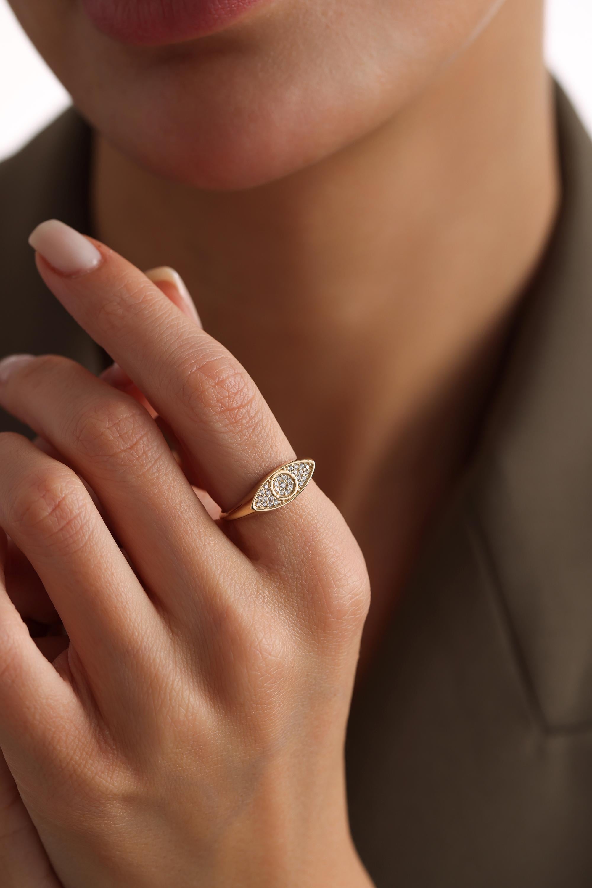 A close-up of a person's hand wearing a gold ring with a diamond-encrusted eye design.