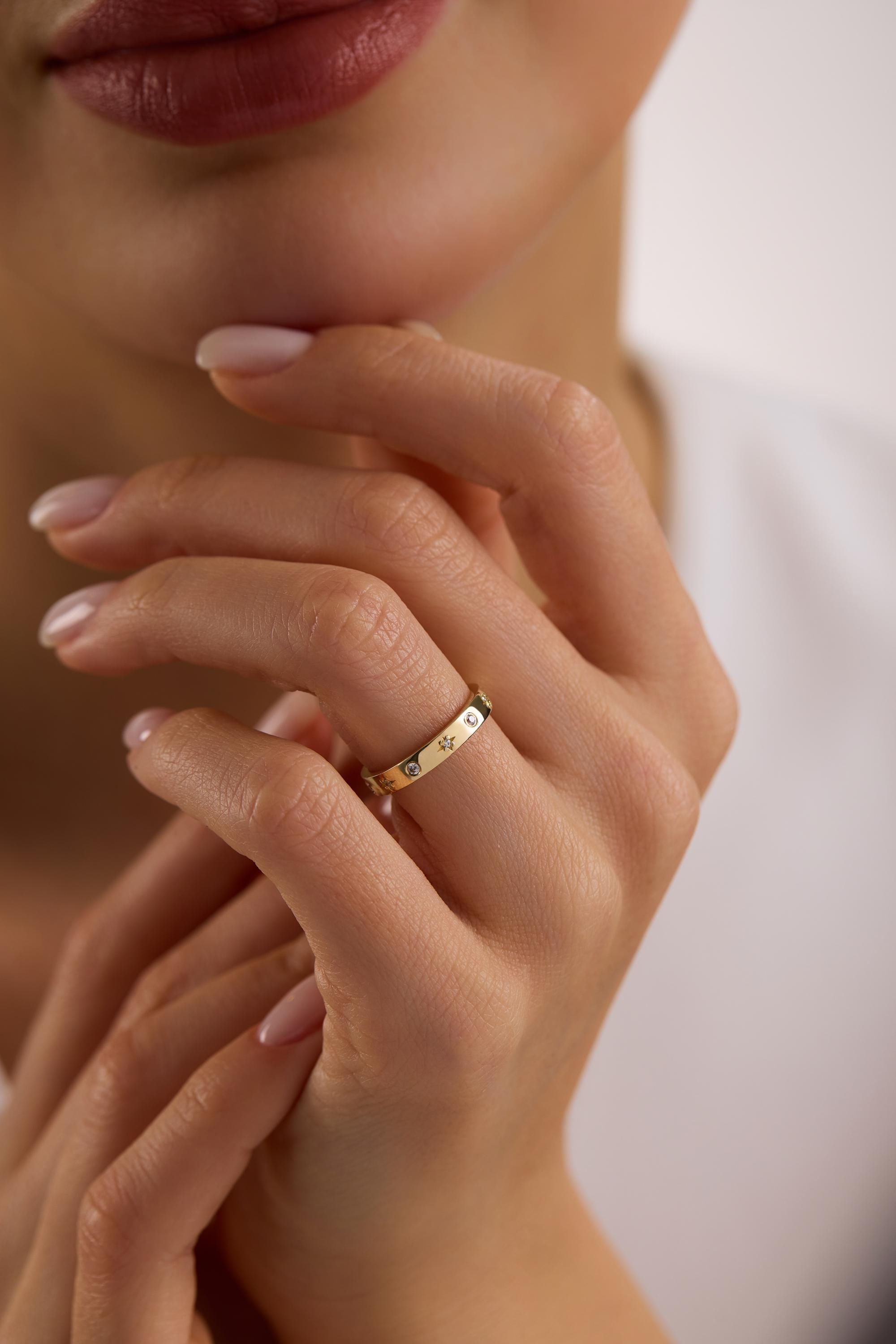 May include: A gold ring with a series of small, clear gemstones and decorative paw prints. The ring is worn on a finger, with the hand resting near the face. The ring is a simple band design.
