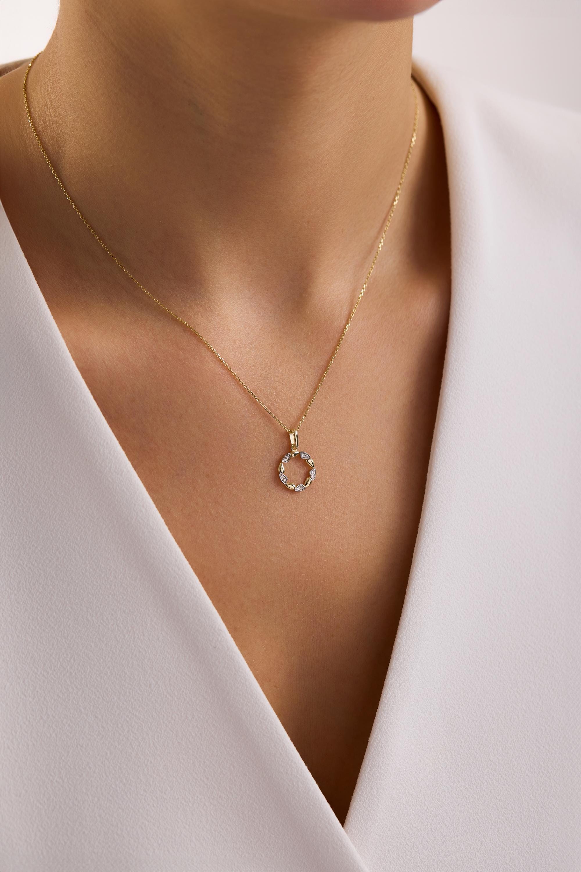 May include: A gold necklace with a small, circular pendant. The pendant is adorned with small, sparkling stones. The necklace is displayed against a white background, highlighting the jewelry's design and color.