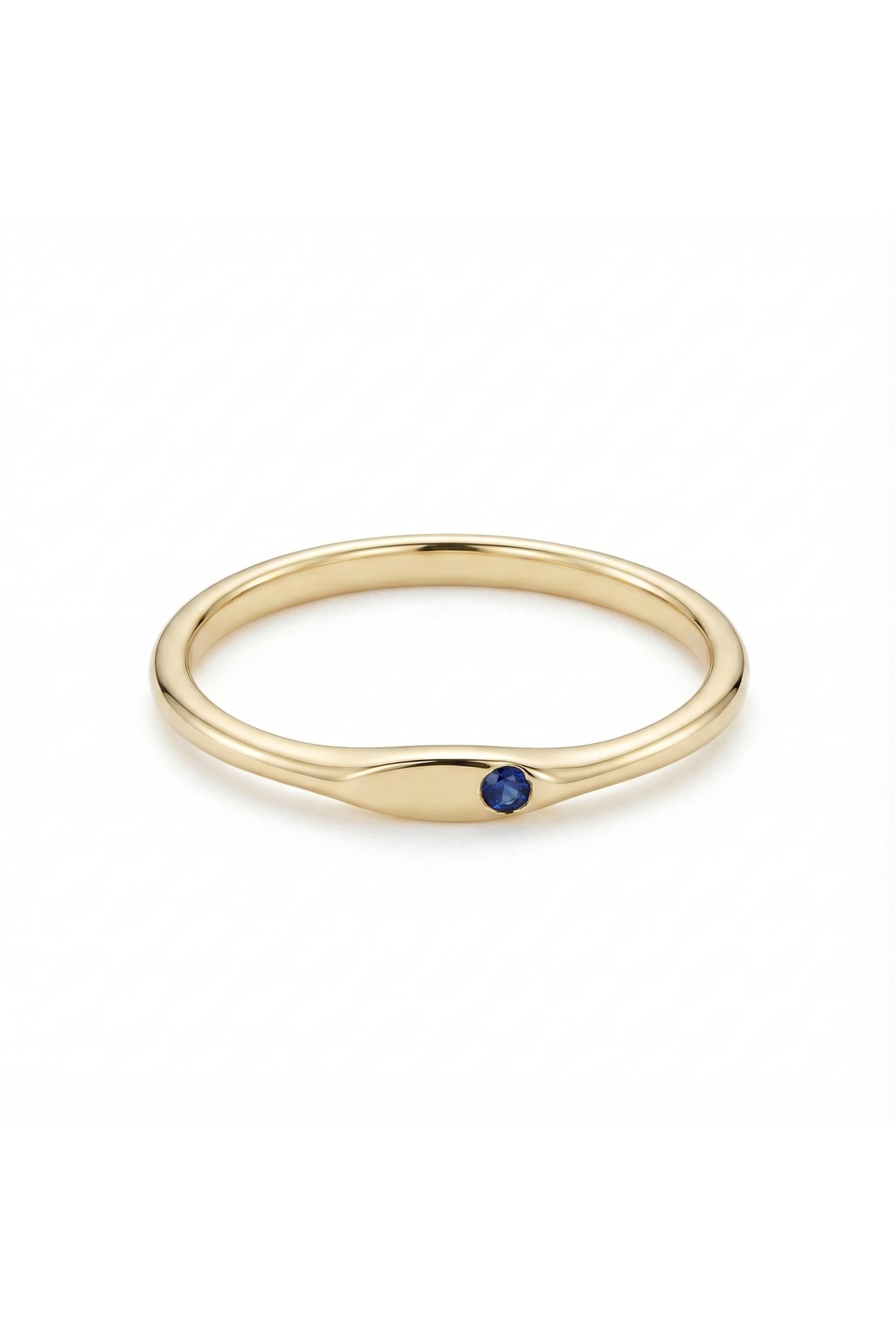 May include: A gold ring with a small, round, dark blue gemstone set in a smooth, elongated bezel. The ring has a simple, elegant design, perfect for everyday wear. The band is a polished gold color.