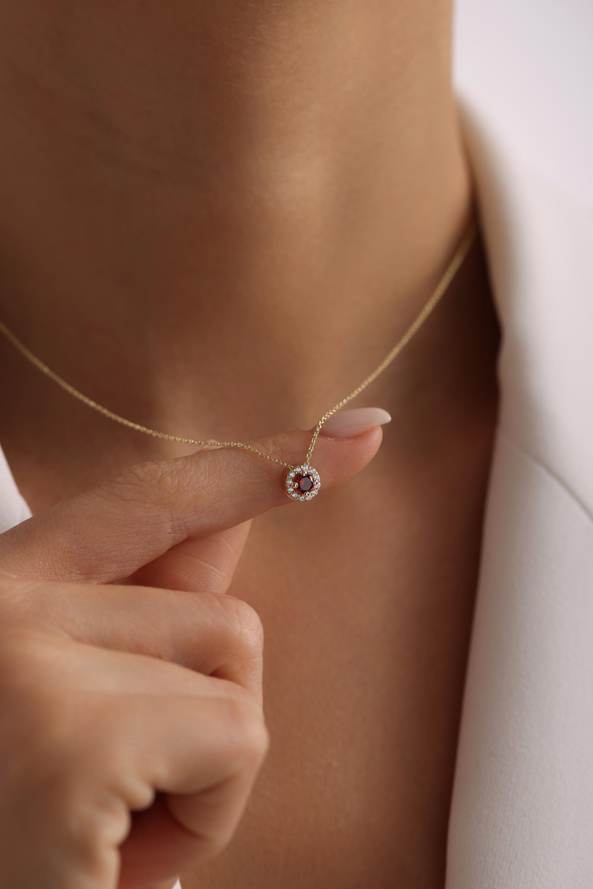 May include: A gold necklace with a small pendant featuring a red gemstone surrounded by a halo of smaller white gemstones.