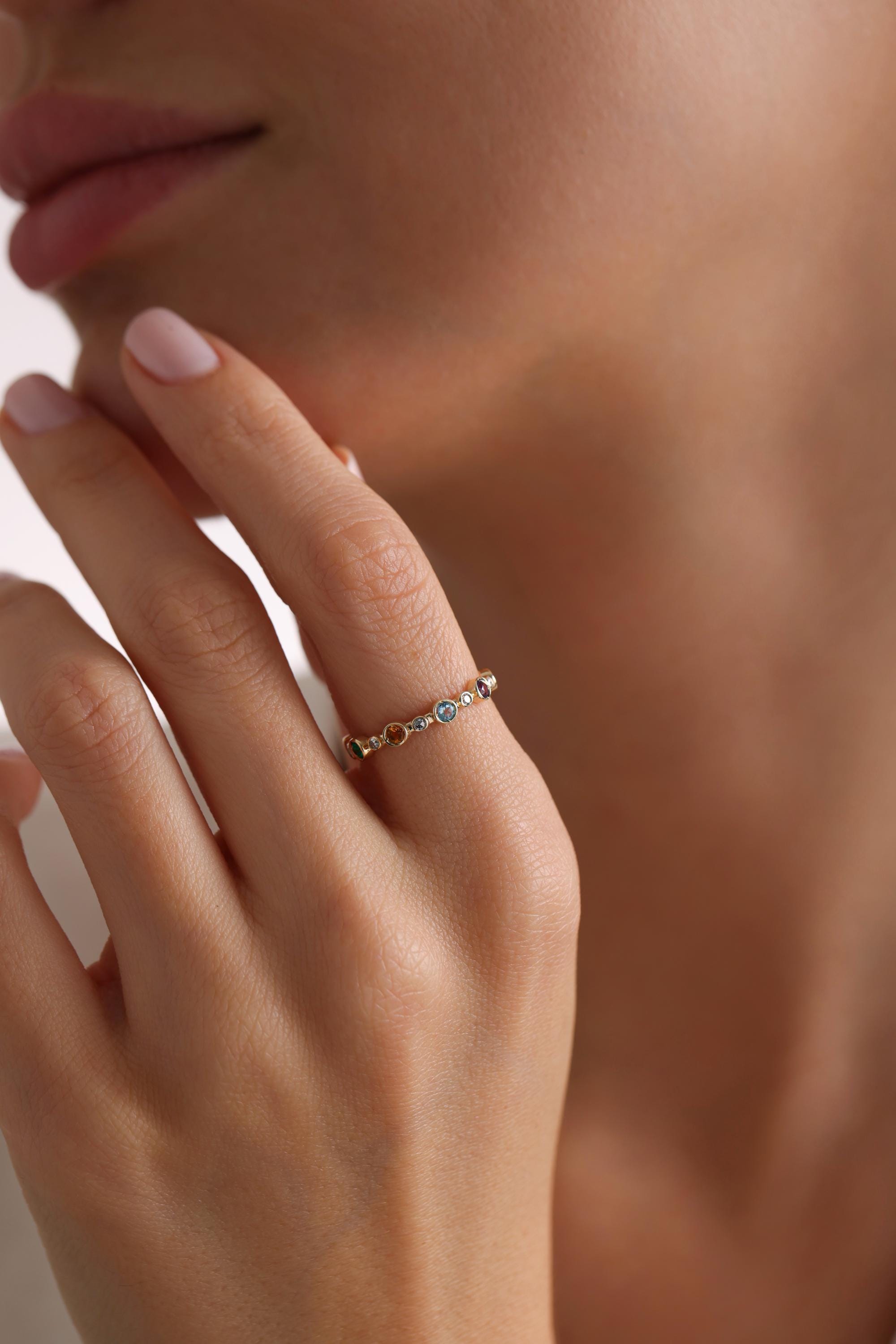 May include: A gold band ring with a row of colorful gemstones. The gemstones are round and appear to be blue, green, orange, red, and purple.