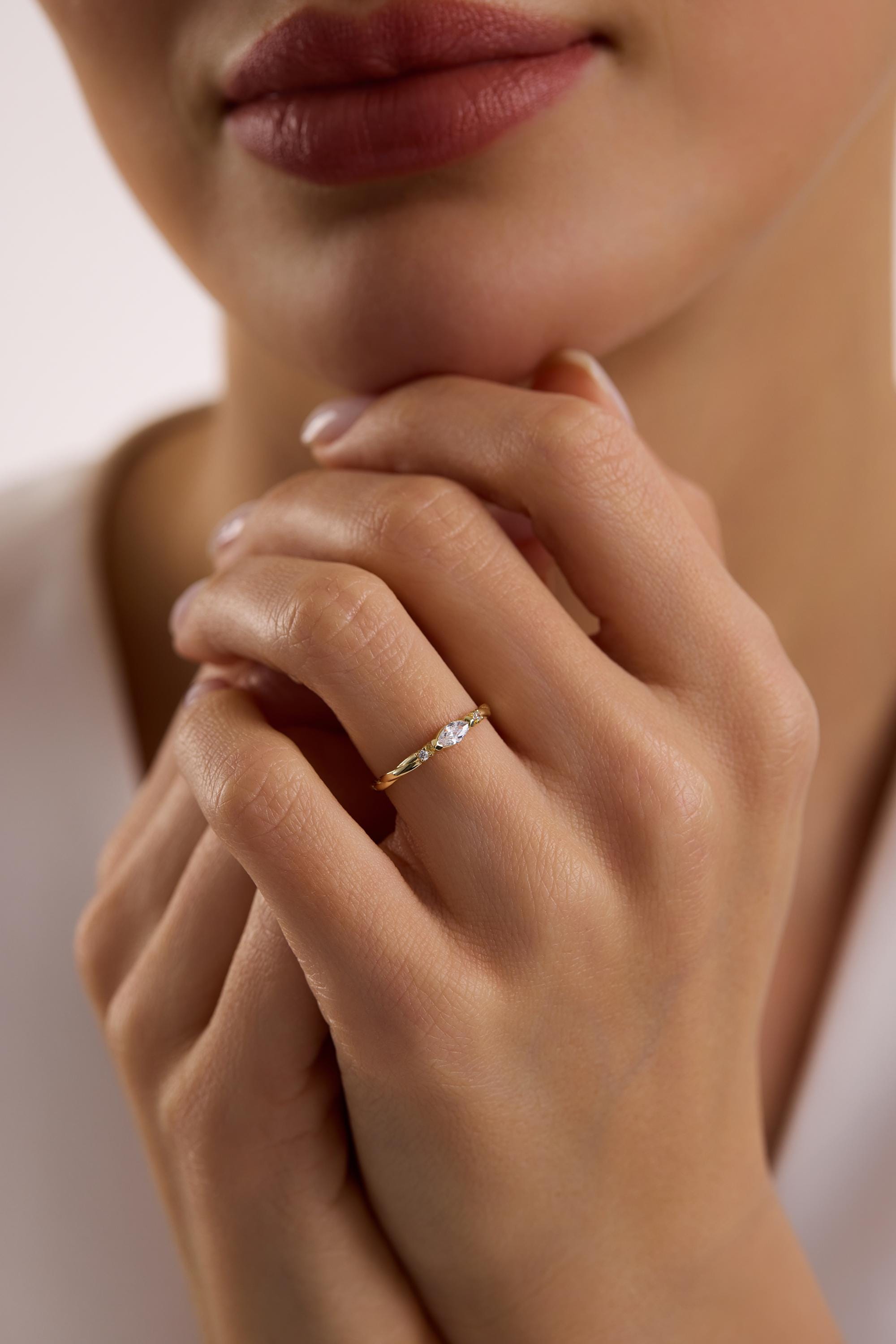 May include: A gold ring with a small, oval-shaped gemstone at the center. The band features a twisted design with small, sparkling accents. The ring is worn on a finger, showcasing its delicate details and elegant style.