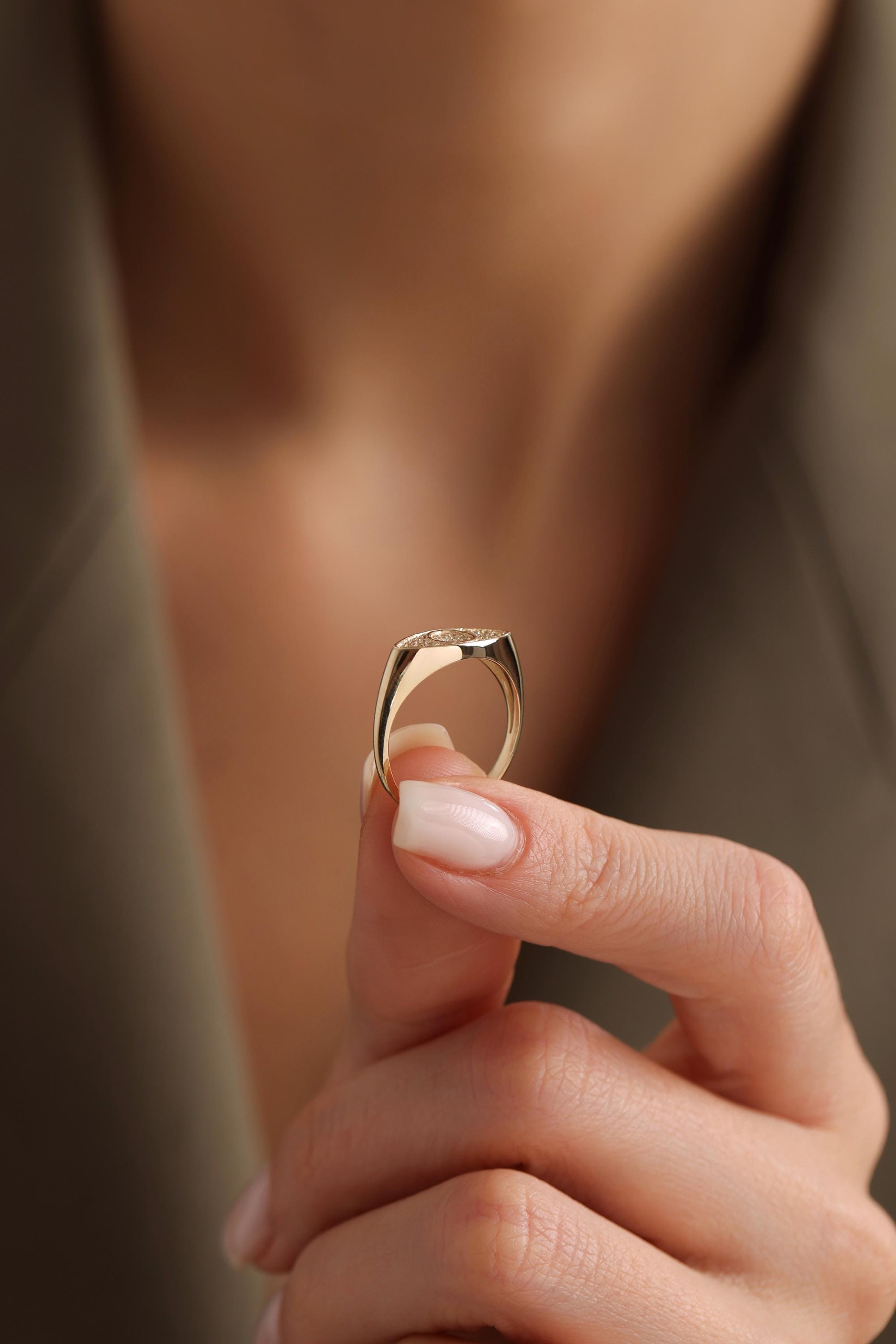 A close-up image of a person's hand holding a gold ring with a diamond in the center.